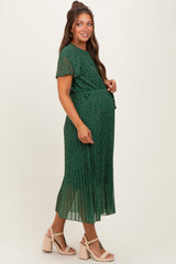 woman wearing a green floral maternity dress with short sleeves and a pleated skirt, holding her baby bump