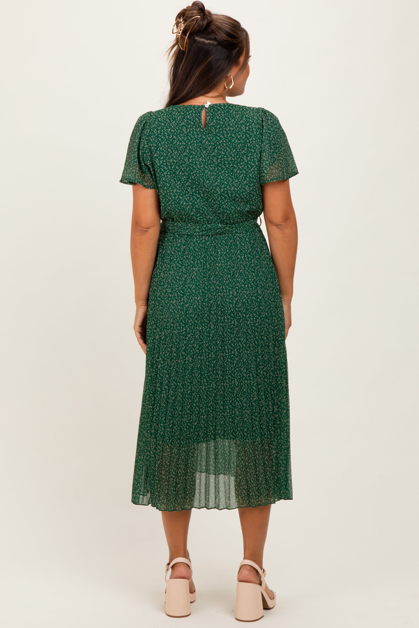 woman wearing a green maternity dress with a floral pattern and pleated skirt, showing her baby bump from the back