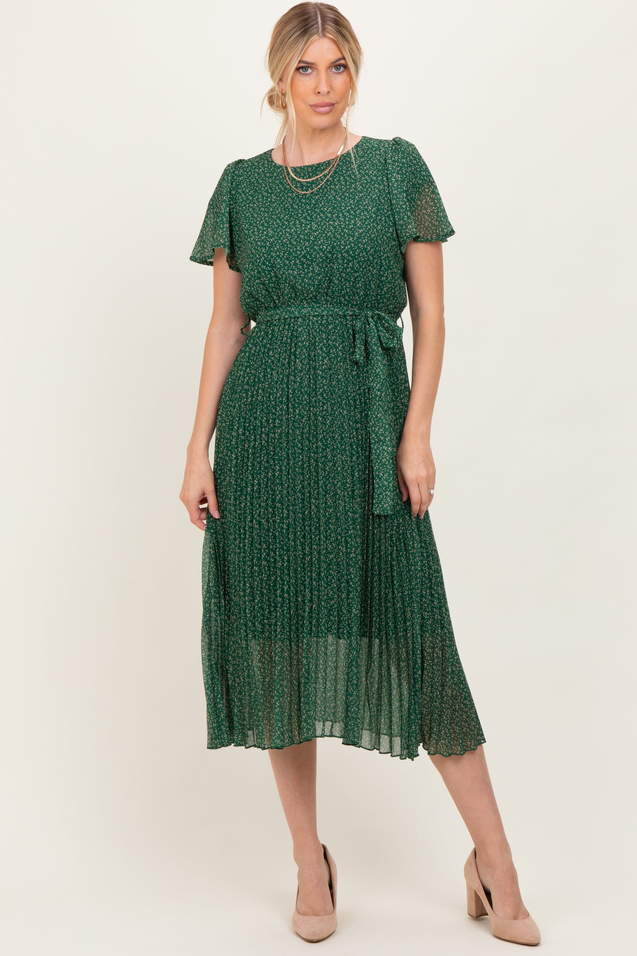 woman wearing a green floral midi dress with short sleeves and a tie waist, styled with nude heels and layered necklaces