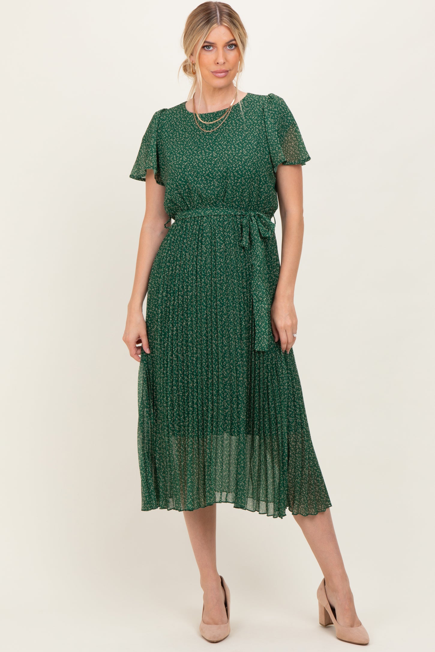 woman wearing a green floral midi dress with short sleeves and a tie waist, styled with nude heels and layered necklaces