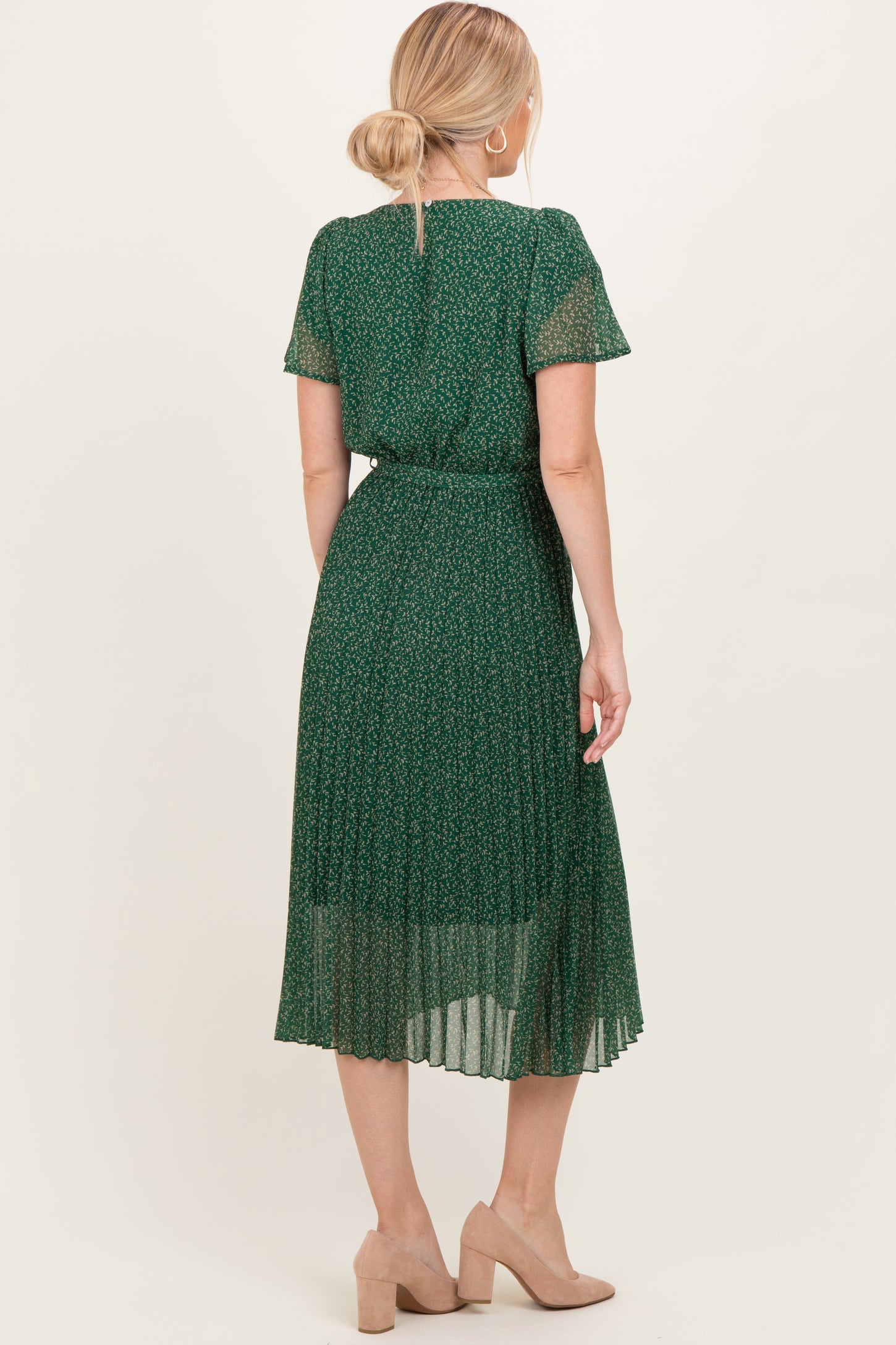 woman wearing a green floral pleated midi dress with short sleeves and a tie waist detail