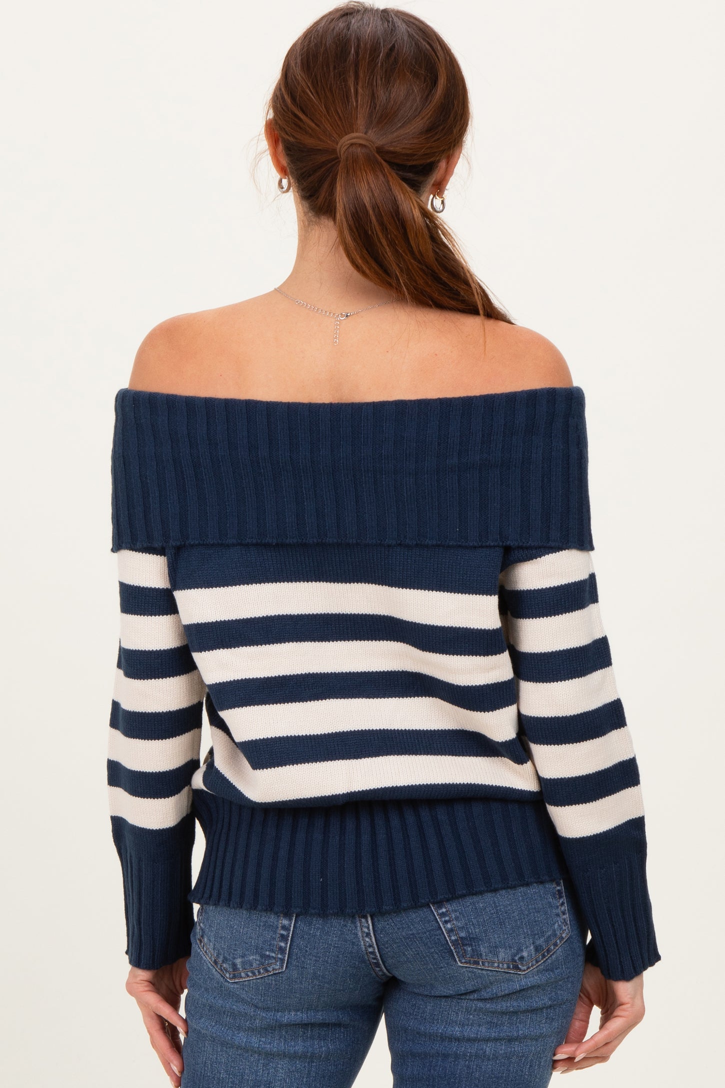 woman wearing a navy and cream striped off-the-shoulder sweater with ribbed detailing and fitted cuffs