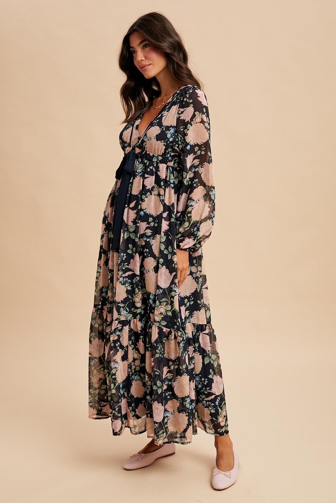 woman wearing a long sleeve floral maxi dress with a deep v-neck and tiered skirt, standing against a beige background