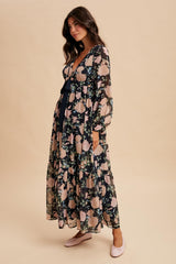 woman wearing a long sleeve floral maxi dress with a deep v-neck and tiered skirt, standing against a beige background