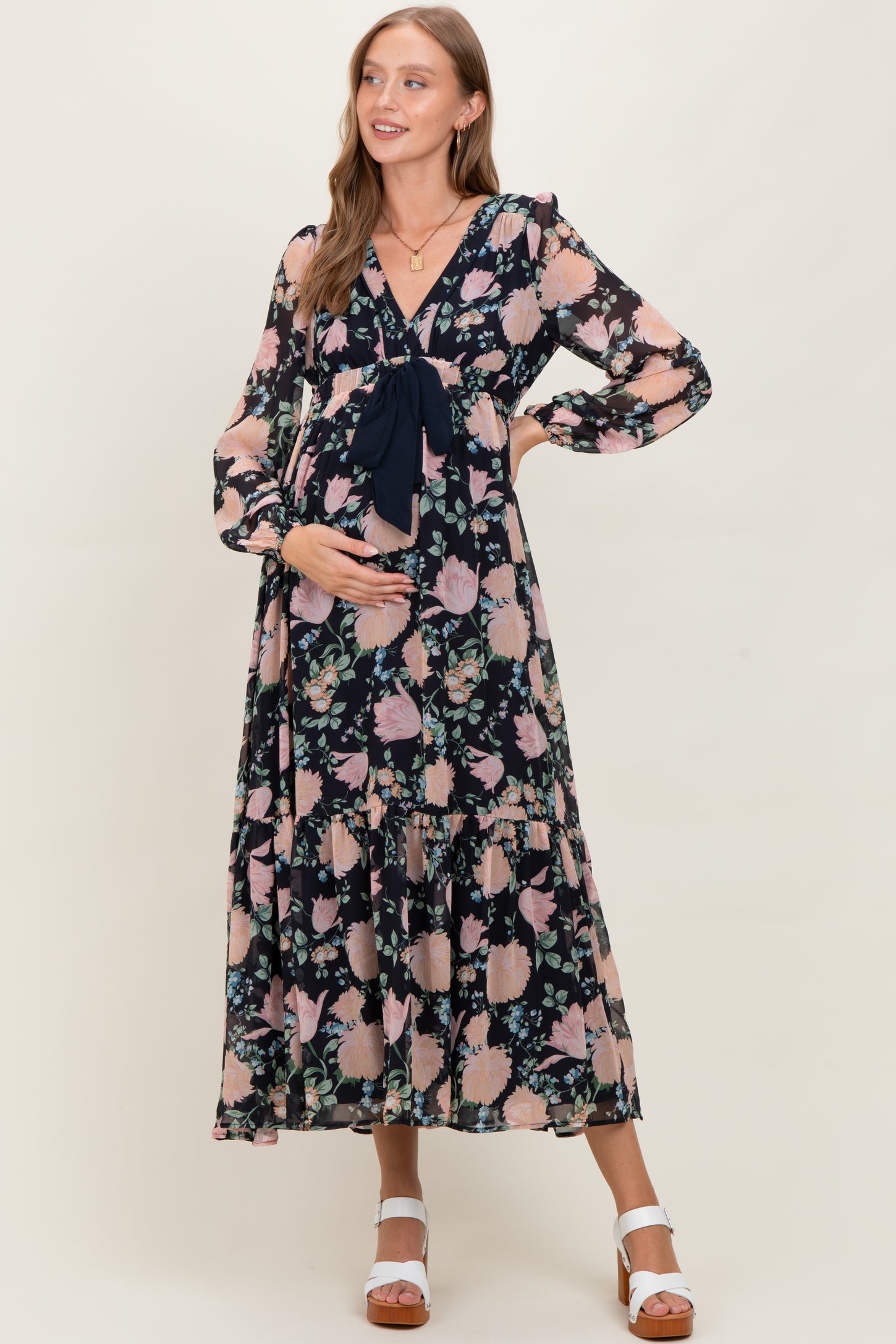 woman wearing a floral navy maternity dress with a tie detail and long sleeves, holding her baby bump