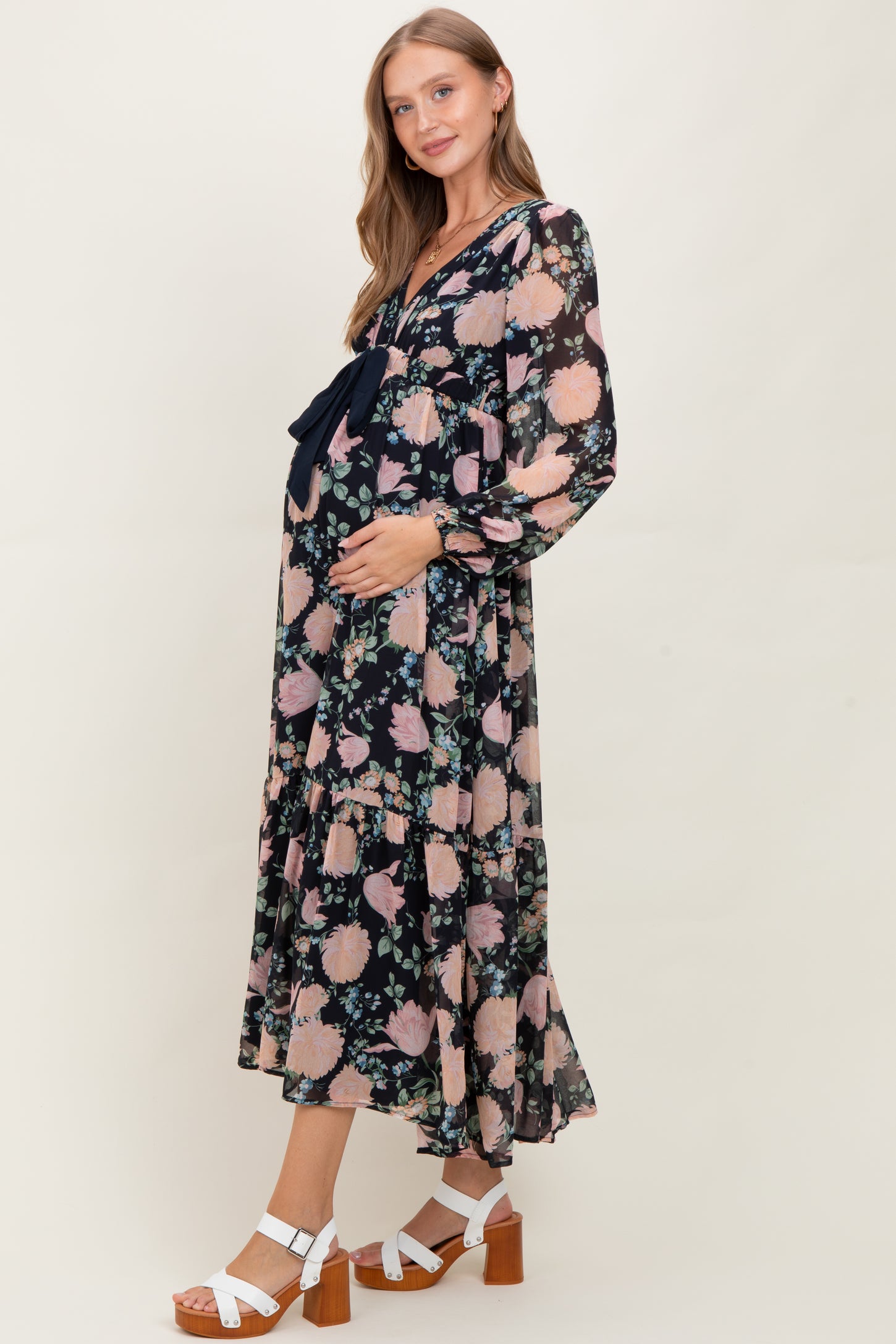 woman wearing a floral maternity dress with a deep v-neck and ruffle hem, holding her baby bump