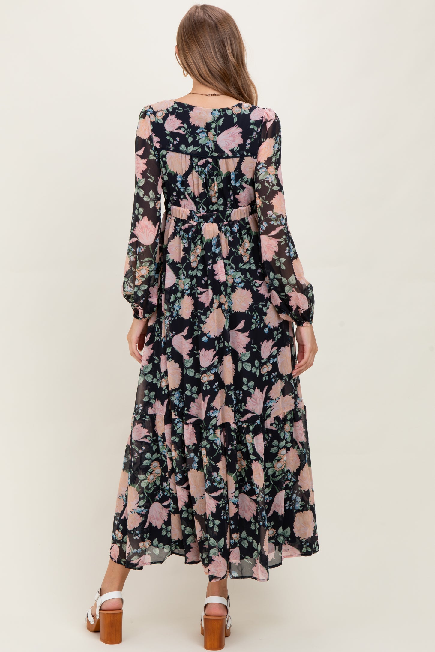 woman wearing a long sleeve black floral maternity maxi dress with ruffles and a baby bump visible from the back