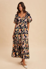 woman wearing a navy floral maxi dress with puff sleeves and a tiered skirt, standing against a neutral background