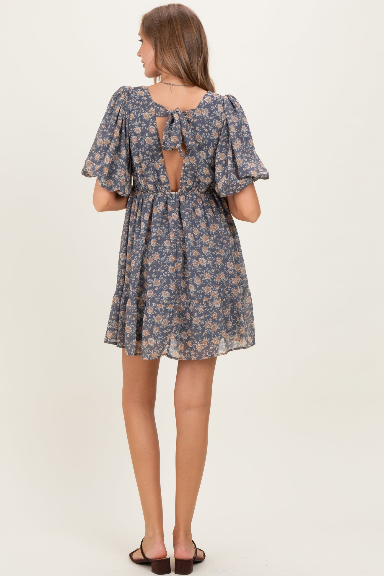 woman wearing a blue floral maternity dress with a back tie detail and ruffled sleeves, showing a baby bump
