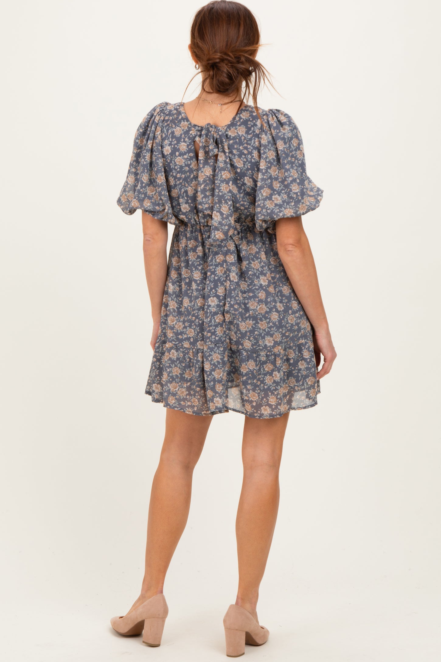 woman wearing a floral short sleeve dress in blue with a cinched waist and back tie detail