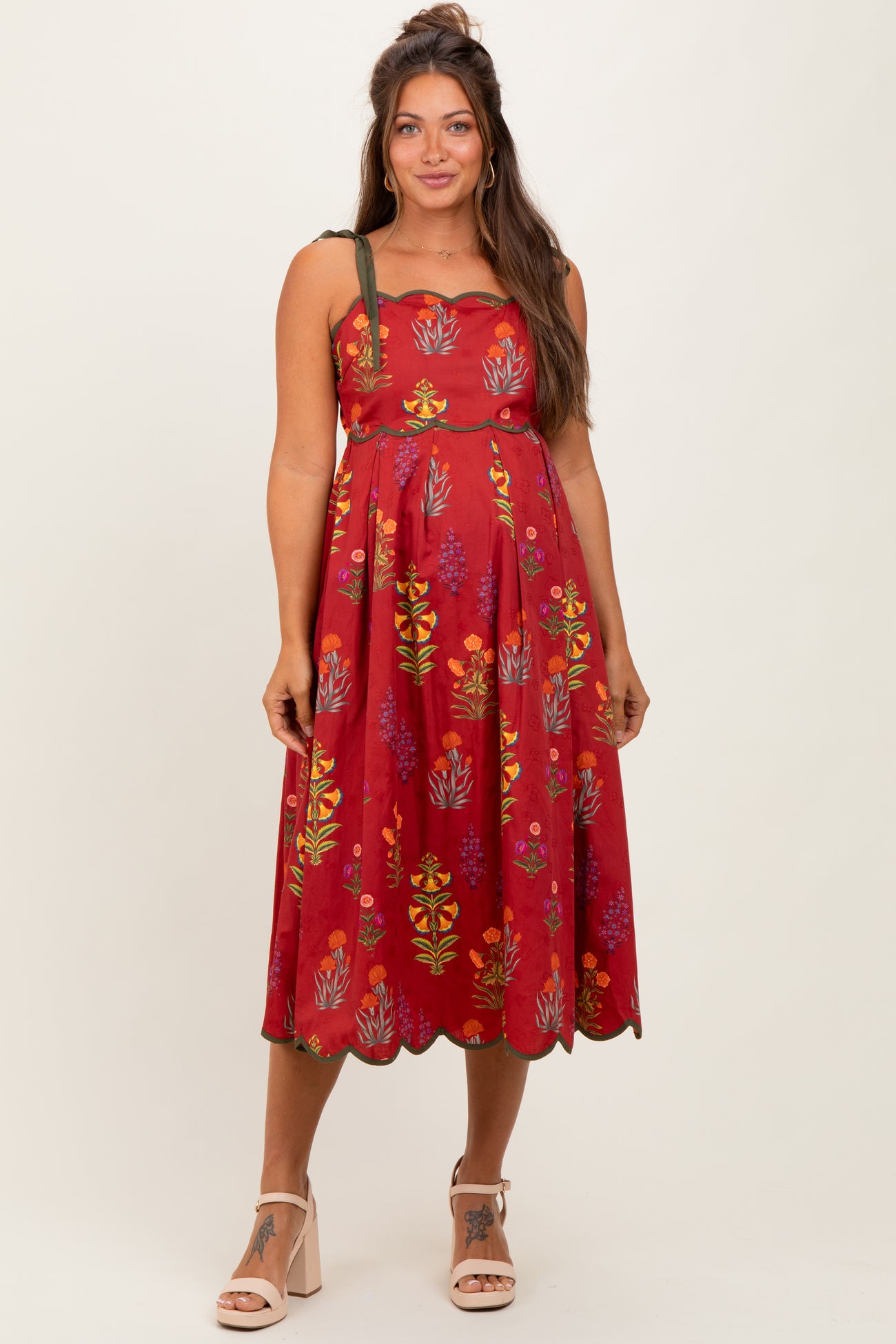 woman wearing a red floral maternity dress with adjustable straps and a flowing skirt, showcasing her baby bump