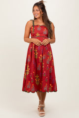 woman wearing a red floral maternity dress with scalloped hem and green straps, smiling at the camera
