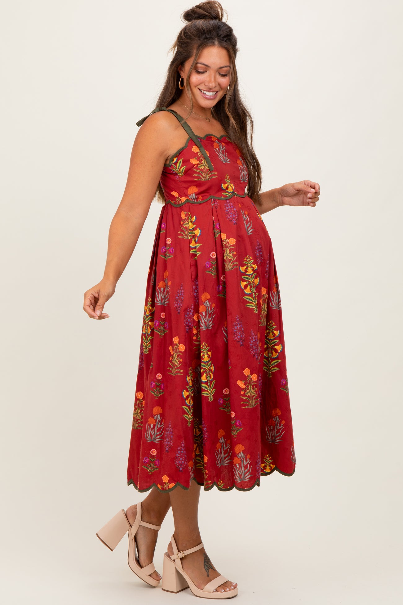 woman wearing a red floral maternity dress with a flowy skirt and a fitted bodice, showcasing her baby bump