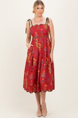 woman wearing a red floral midi dress with scalloped details and tie straps, styled with pockets and nude heels