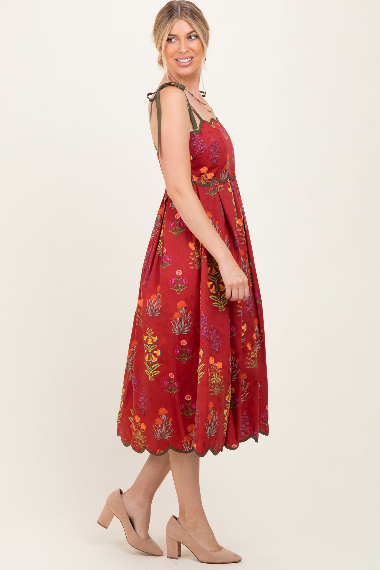 woman wearing a red floral midi dress with adjustable straps and scalloped hem, styled with nude block heels