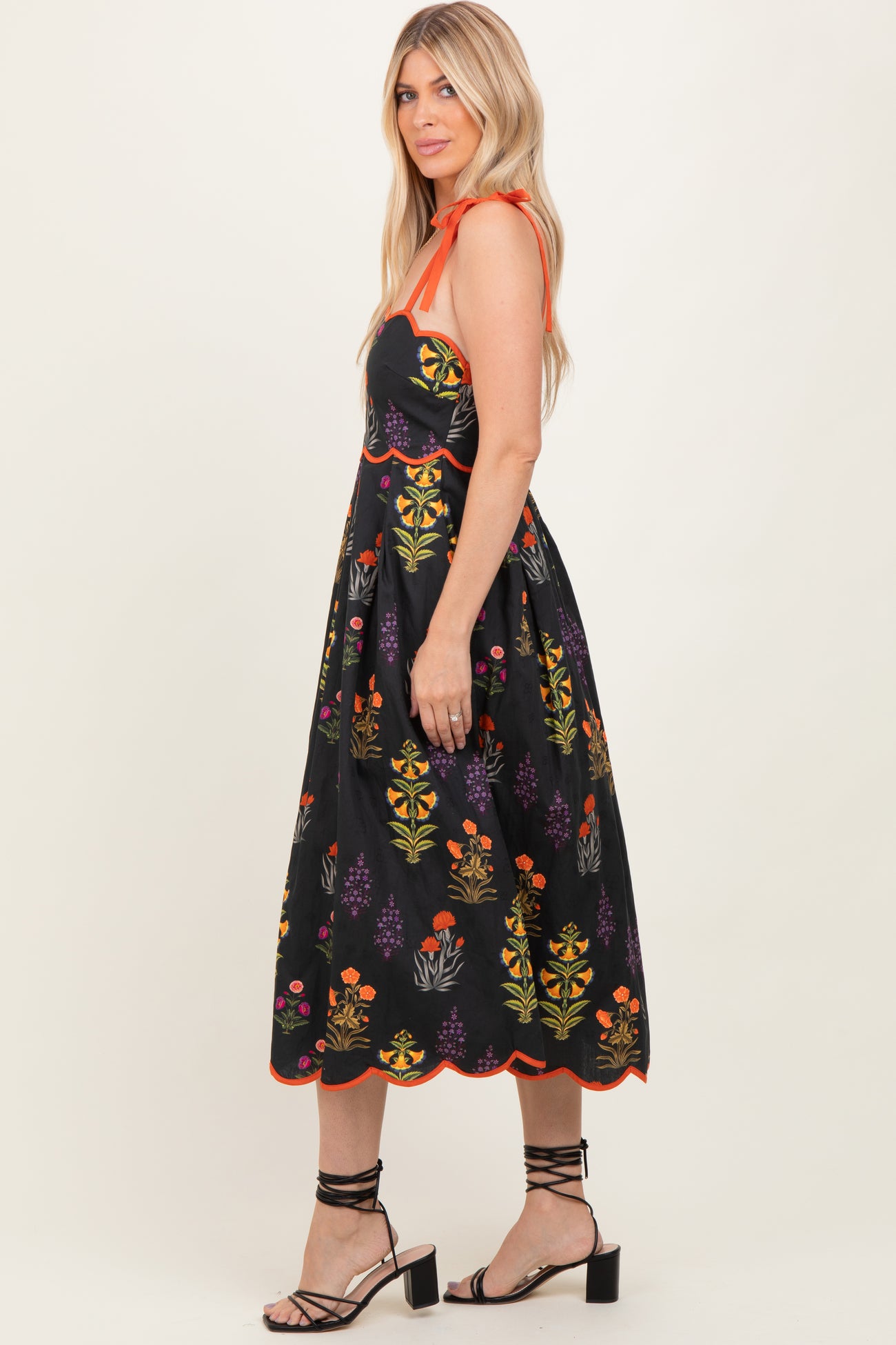 woman wearing a black embroidered sundress with colorful floral designs and orange accents, standing sideways