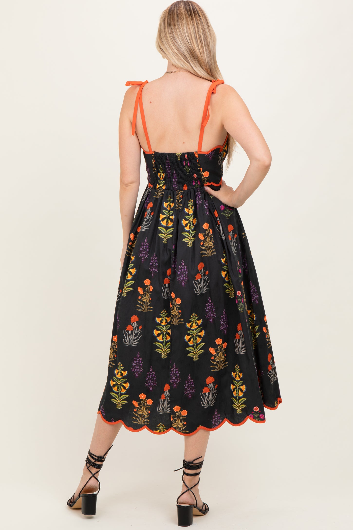 woman wearing a black floral midi dress with adjustable straps and a smocked back, showing a colorful floral pattern