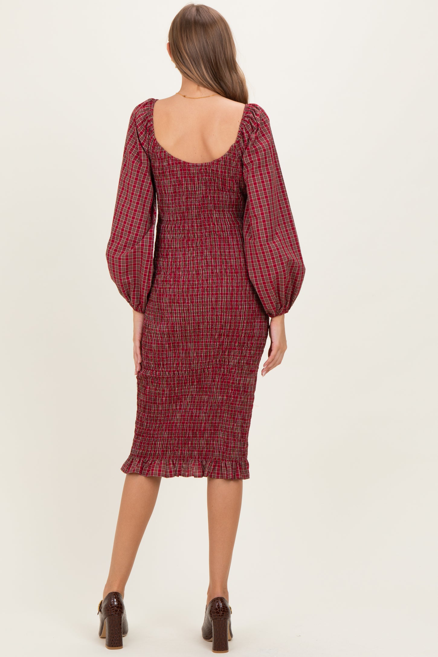 woman wearing a burgundy smocked maternity dress with long puffed sleeves and a midi length