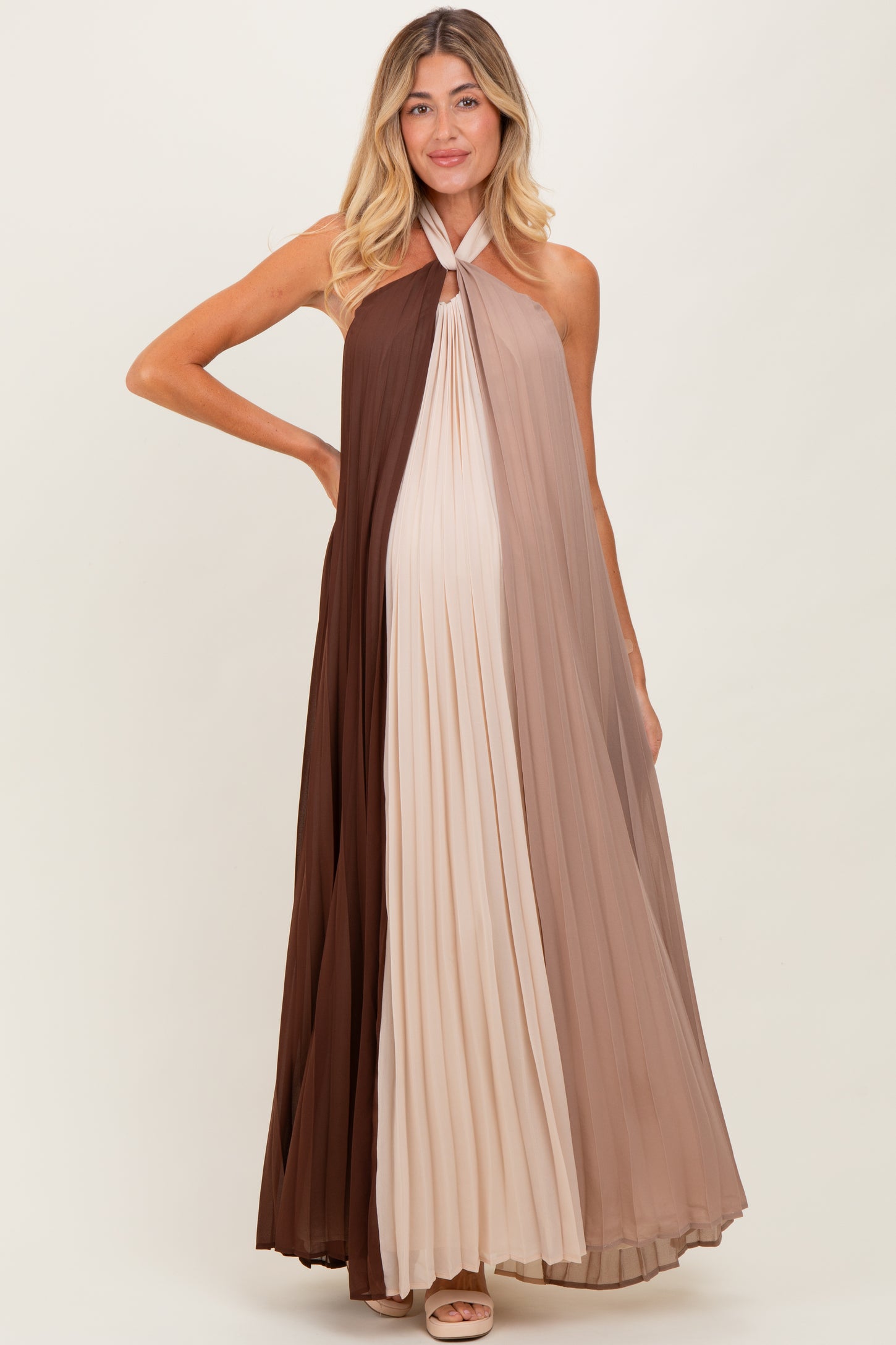 woman wearing a color-blocked pleated maternity dress in shades of brown and beige, showcasing her baby bump