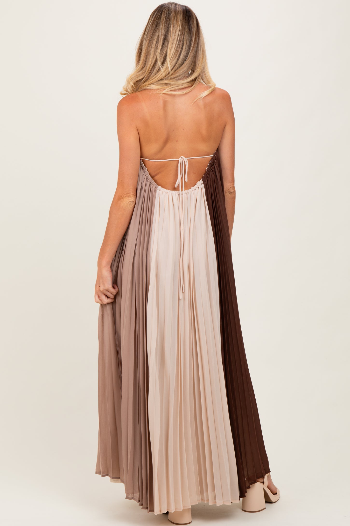 woman wearing a pleated maternity maxi dress in gradient shades of brown and beige, featuring a back tie detail