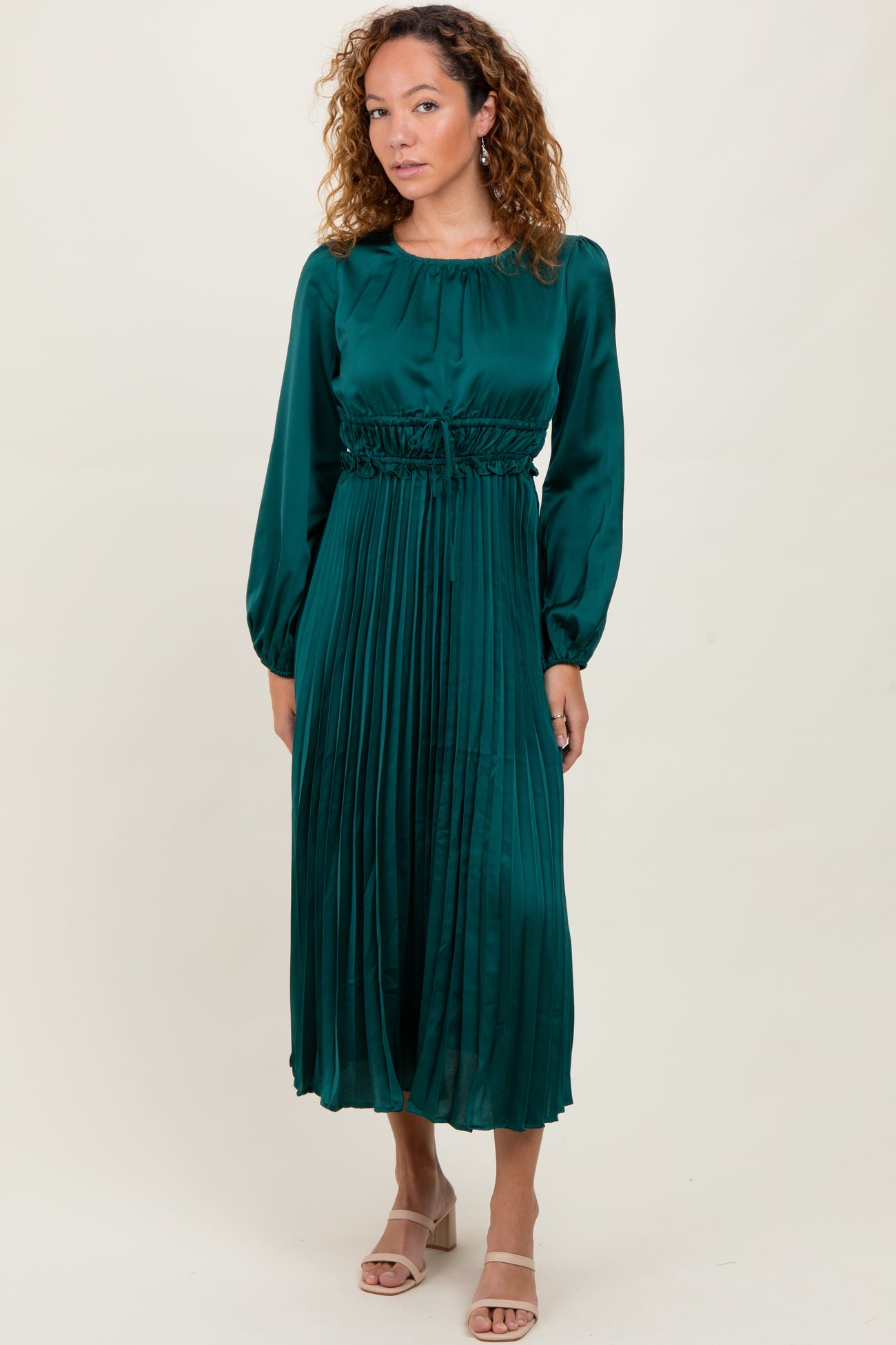 woman wearing a dark green midi dress with pleated skirt and long sleeves, styled with open-toe heels