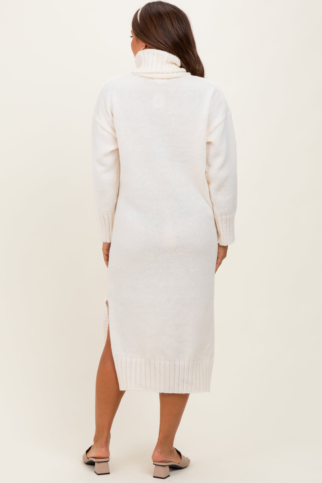 woman wearing a cream-colored maternity sweater dress with a turtleneck and side slits