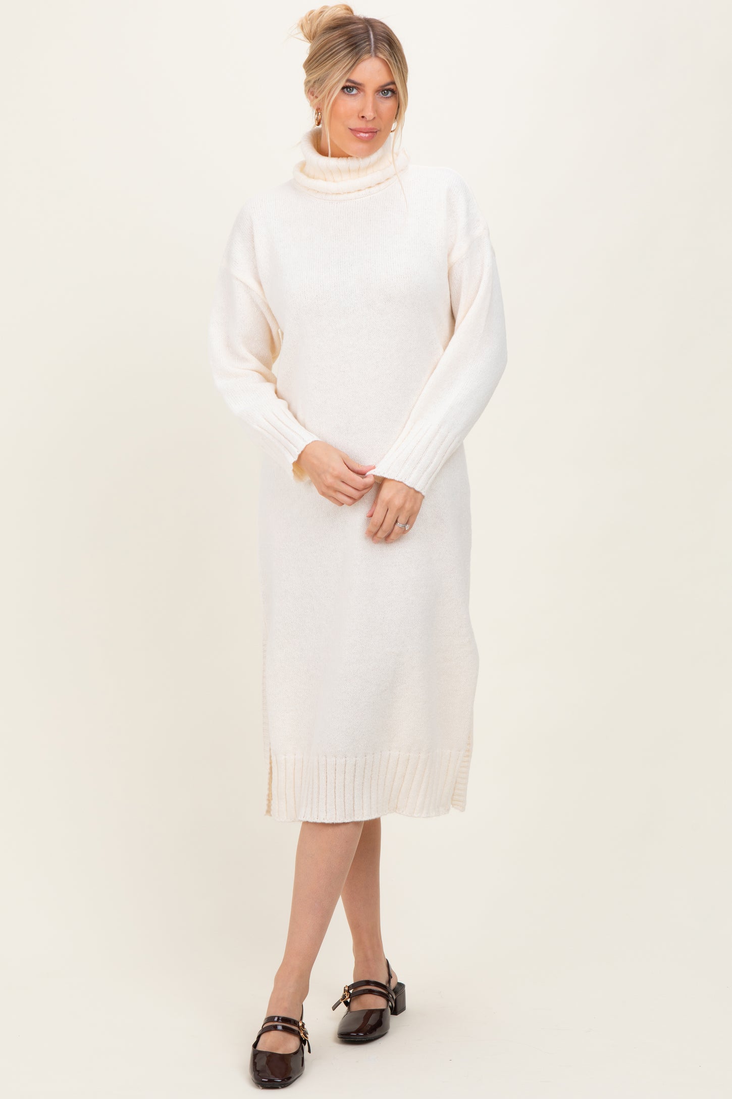 woman wearing a cream-colored long sleeve knit sweater dress with a mock turtleneck and side slits