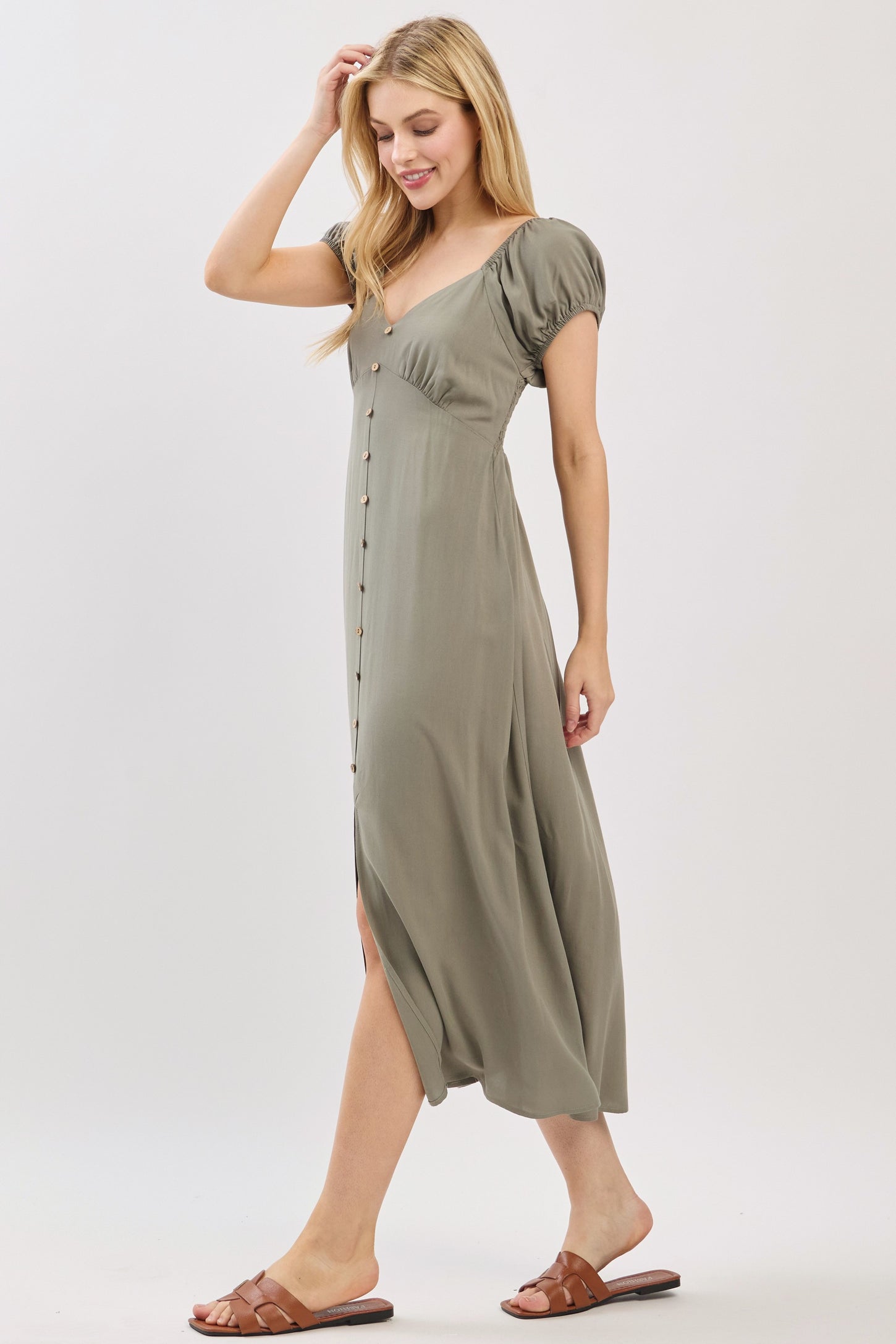 woman wearing a sage green button-up midi dress with puff sleeves and a side slit, walking in sandals