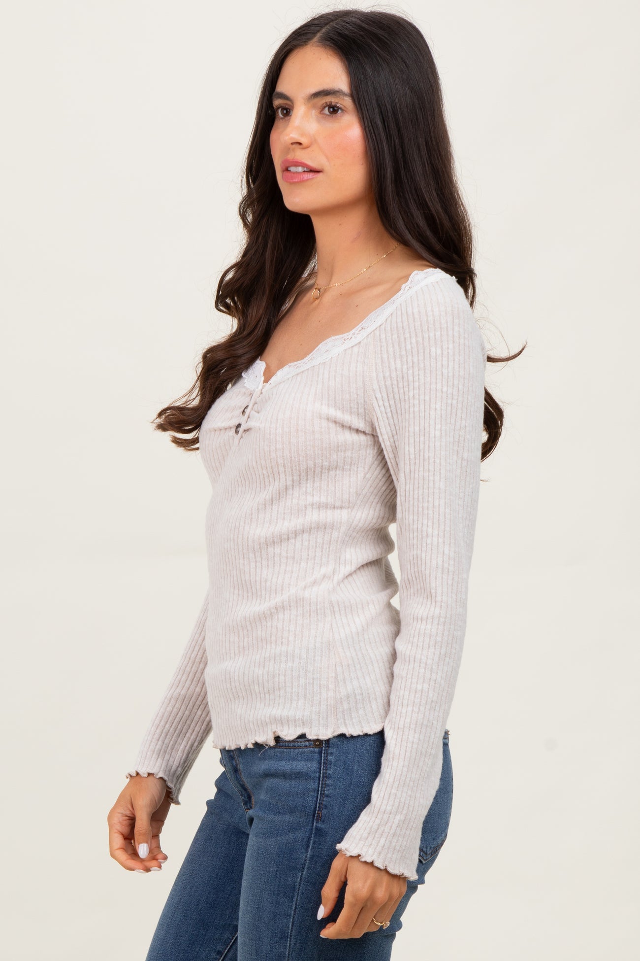 woman wearing a light gray ribbed long sleeve top with a v-neck and lace trim, paired with blue jeans