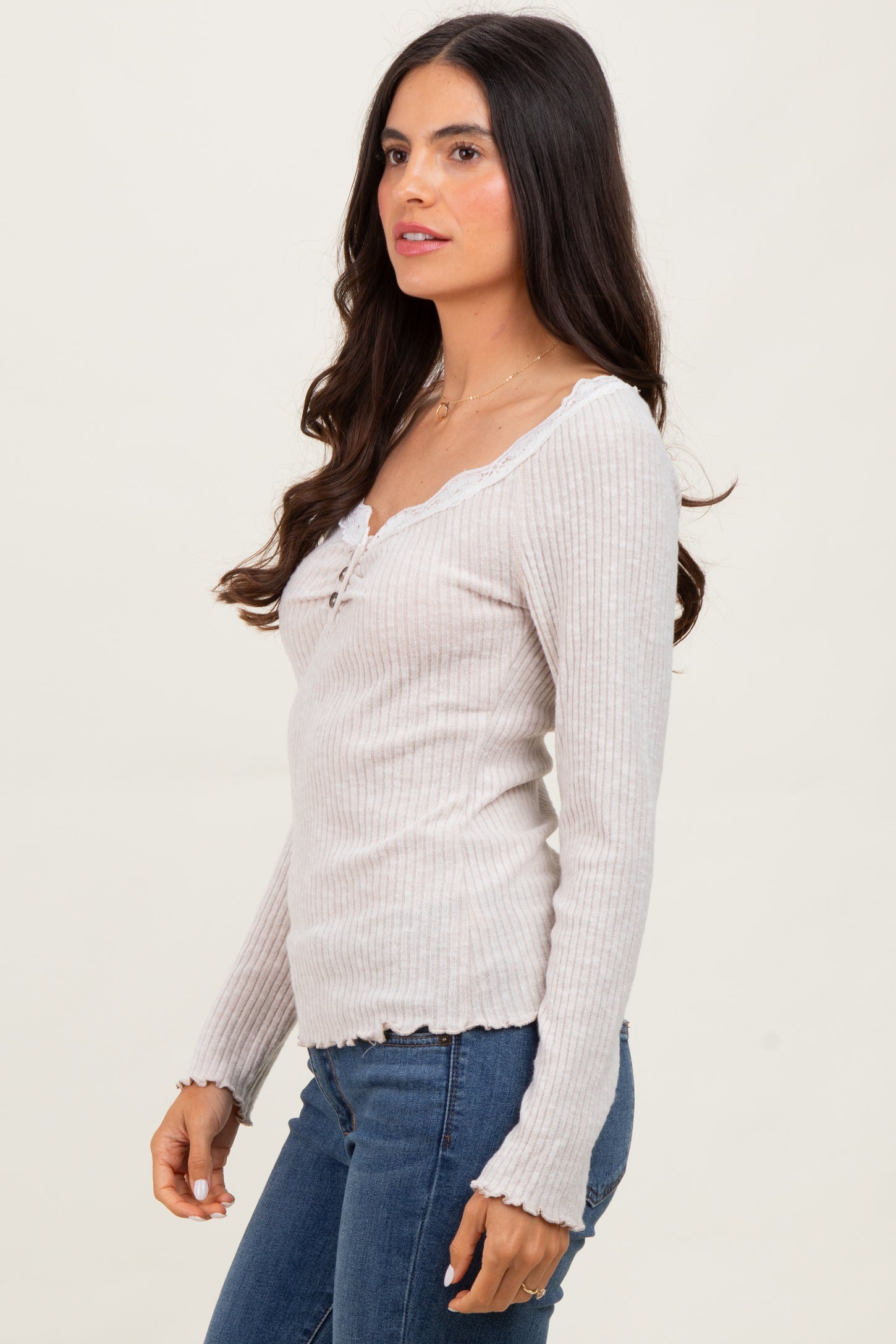 woman wearing a light gray ribbed long sleeve top with a v-neck and lace trim, paired with blue jeans