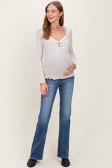 woman wearing a light beige maternity long sleeve top with a henley neckline and scalloped edges, showing her baby bump, paired with flared jeans