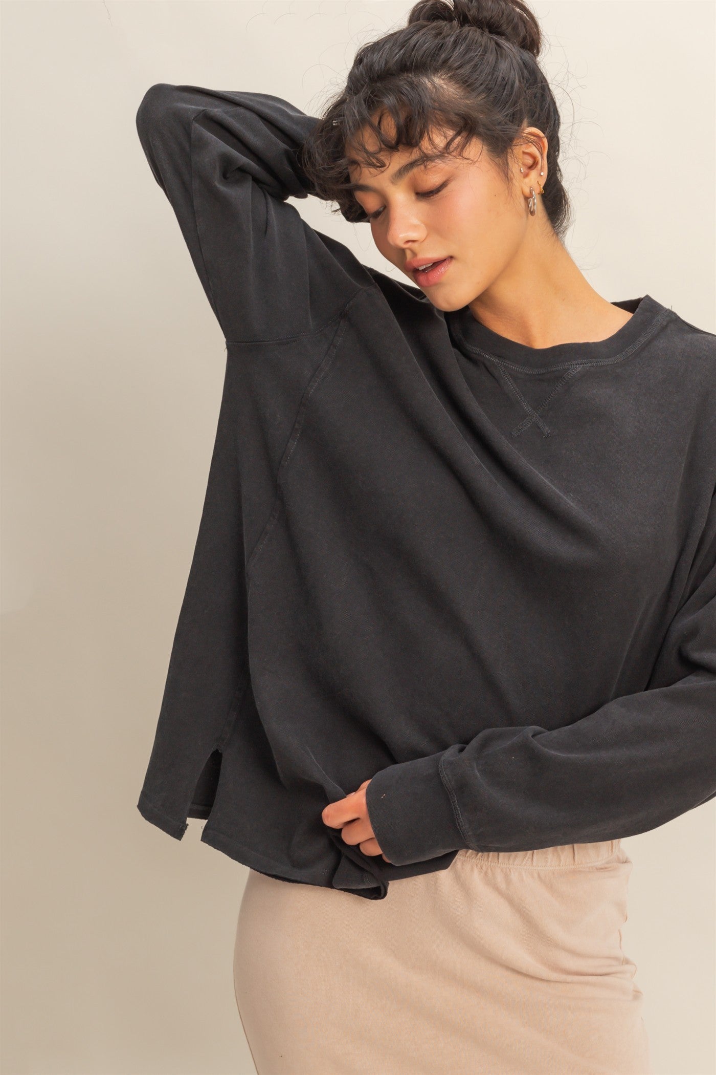 woman wearing a black oversized sweatshirt with dropped shoulders and side slits, paired with a beige skirt