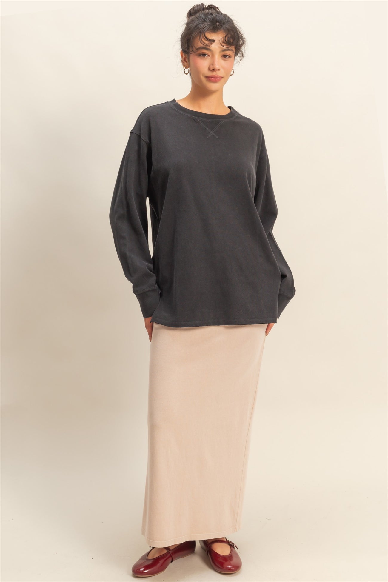 woman wearing a dark gray oversized long sleeve top and a beige maxi skirt, standing with hands in pockets