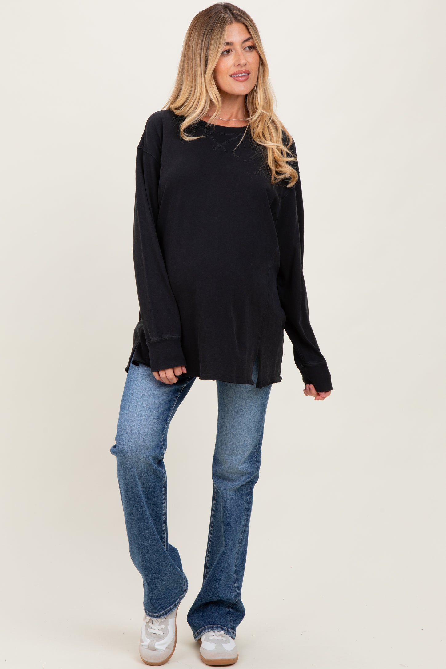 woman wearing a black oversized maternity sweatshirt and blue flared jeans with a baby bump visible