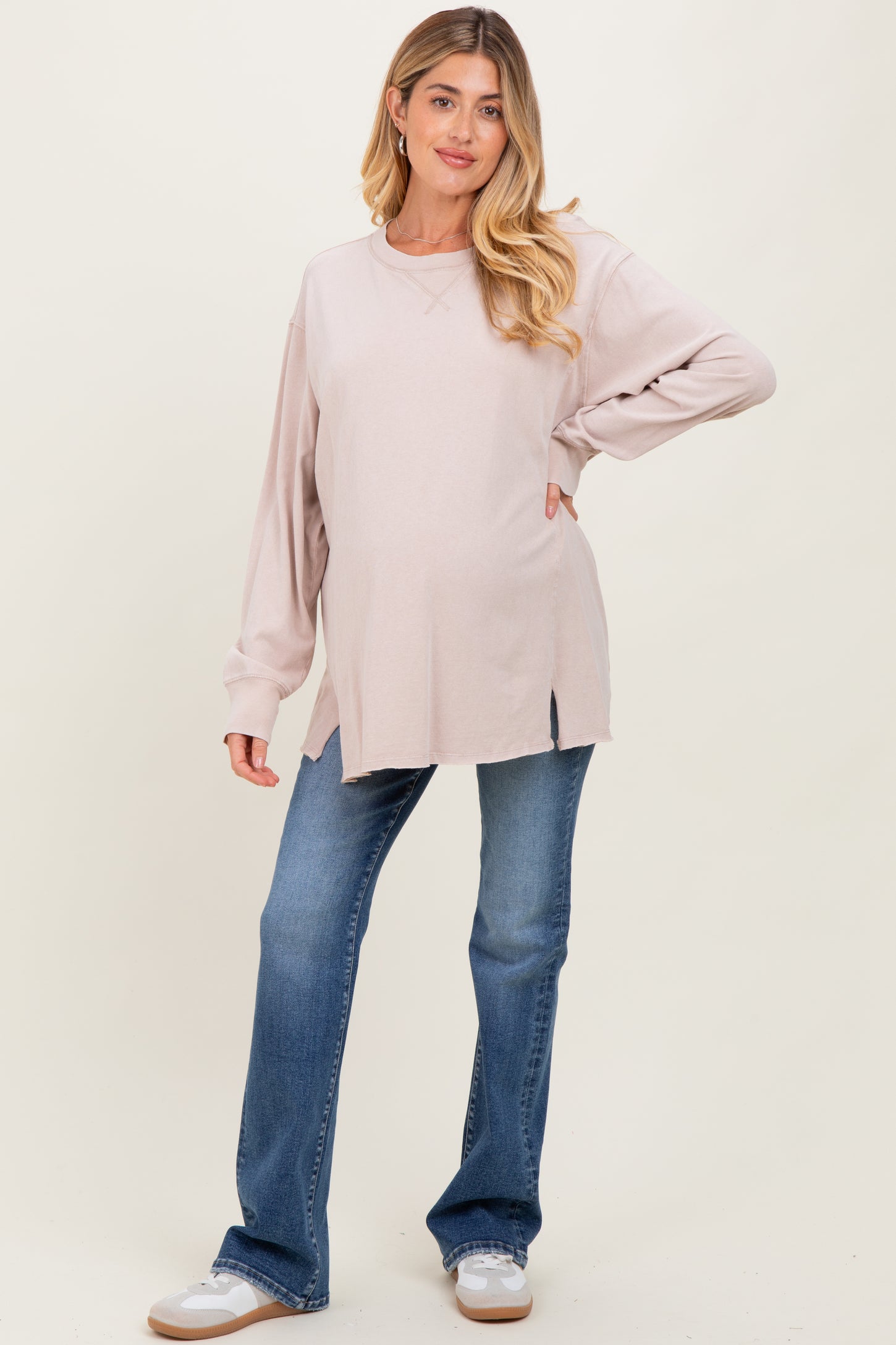 woman wearing a light pink maternity long sleeve top with side slits and blue bootcut jeans, showing her baby bump