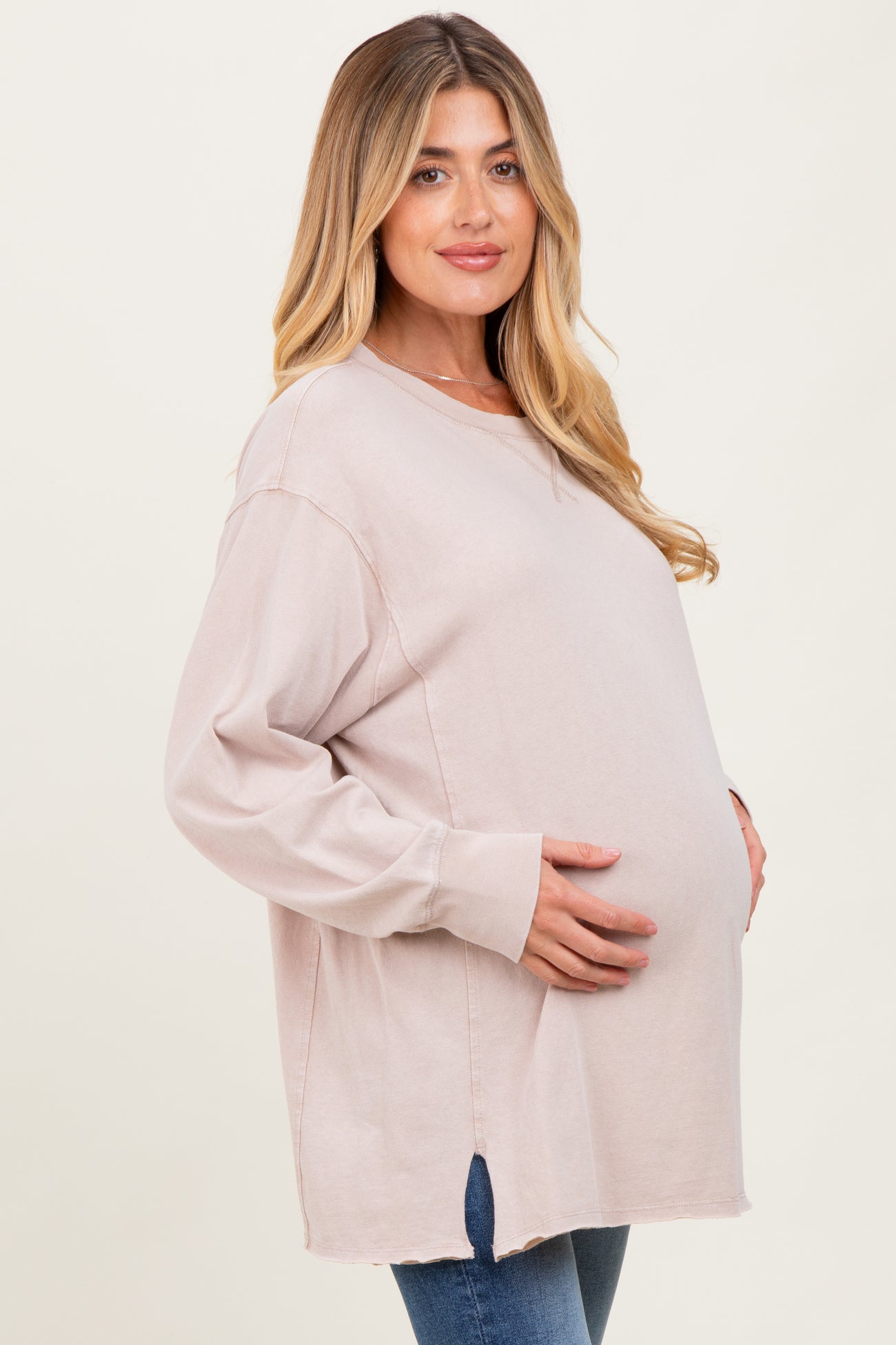 woman wearing a light pink oversized maternity sweatshirt and holding her baby bump