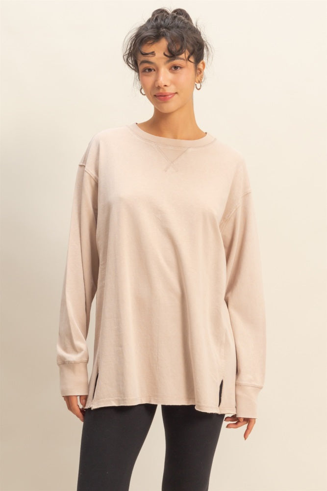 woman wearing a light beige oversized long sleeve top with side slits and a relaxed fit