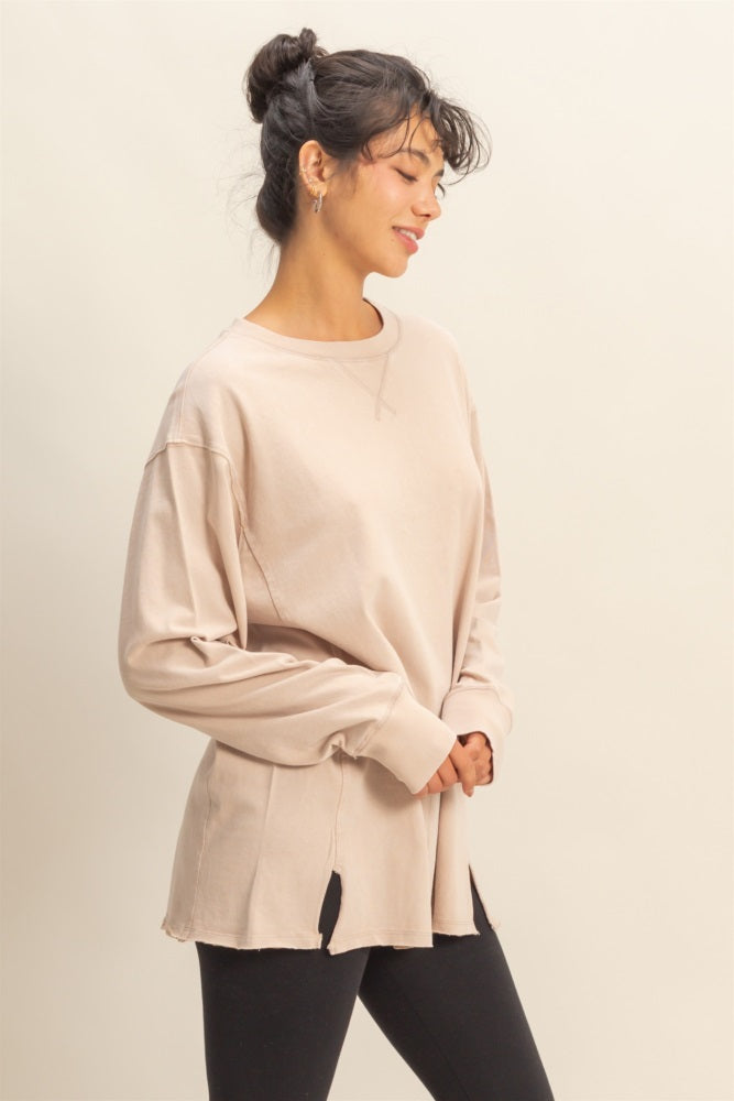 woman wearing a beige long sleeve oversized top with side slits and styled with black leggings