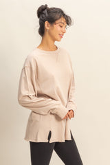 woman wearing a beige long sleeve oversized top with side slits and styled with black leggings