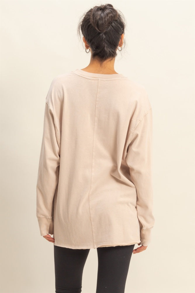 woman wearing a beige long sleeve oversized top with a raw hem and from the back, paired with black leggings