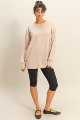woman wearing a beige oversized long sleeve tee with black leggings and black flats