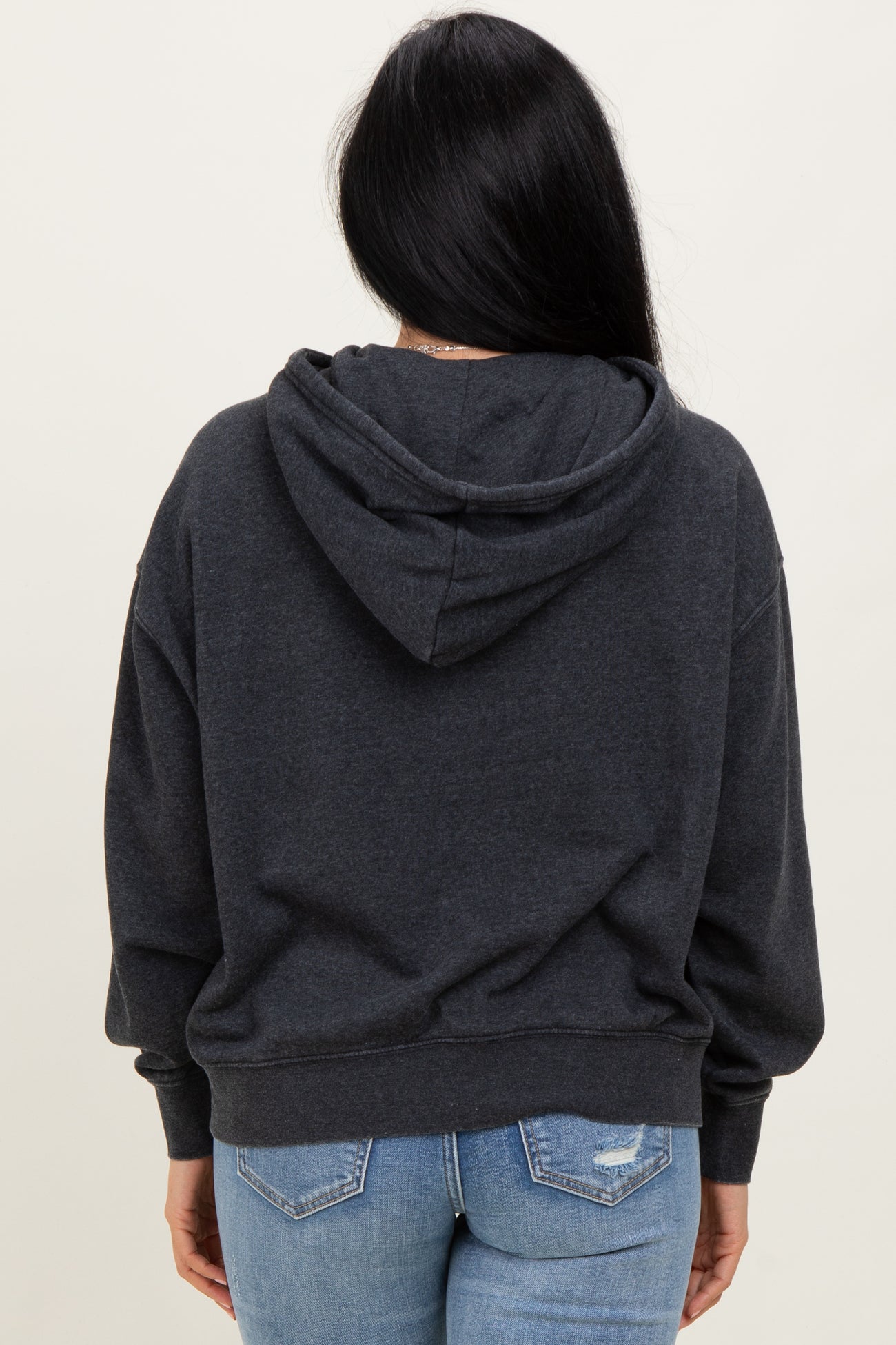 woman wearing a dark gray hoodie from the back with a hood and relaxed fit, paired with light blue jeans