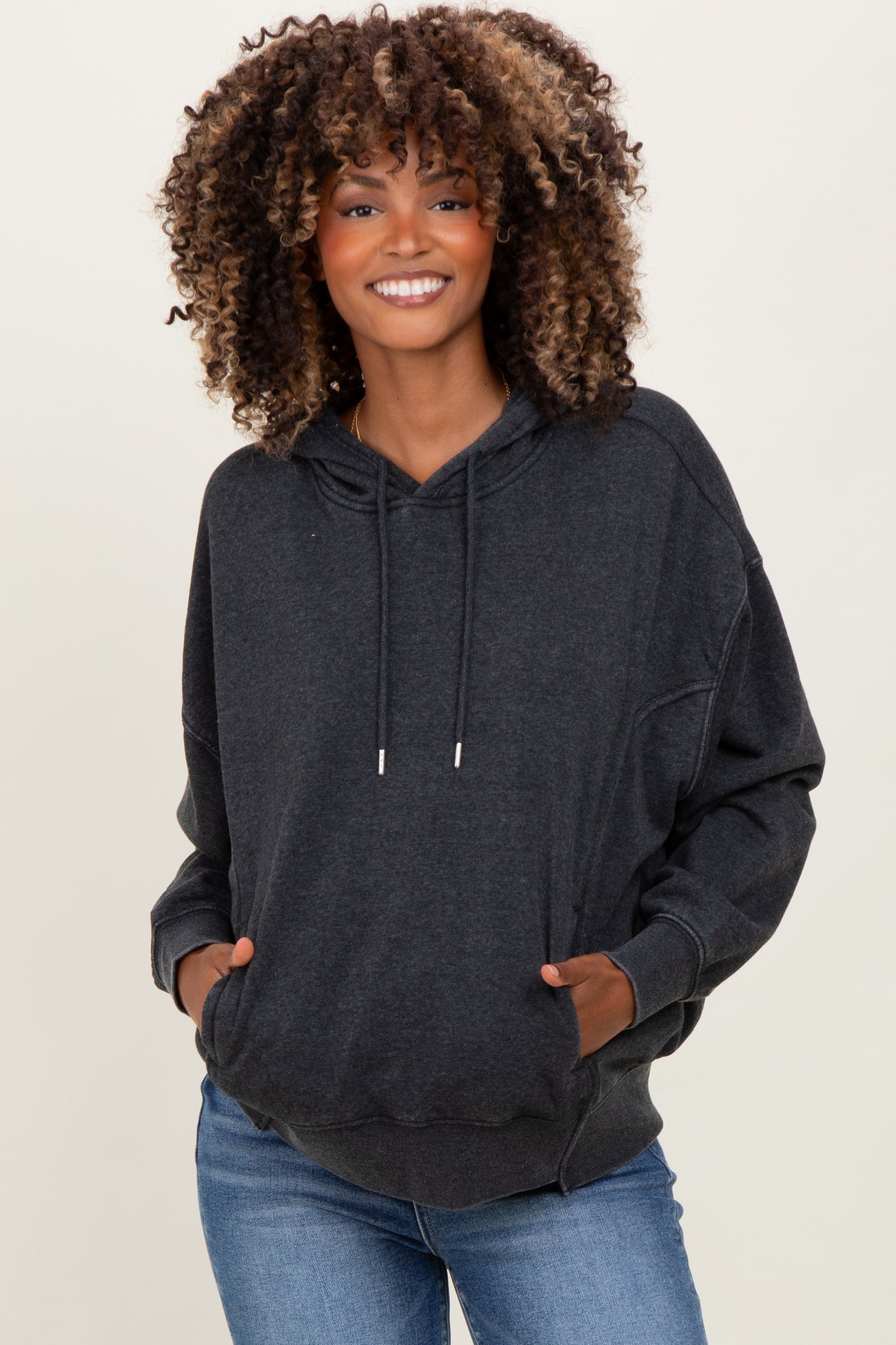 woman wearing a dark gray oversized maternity hoodie with a front pocket and hood, styled with light wash jeans