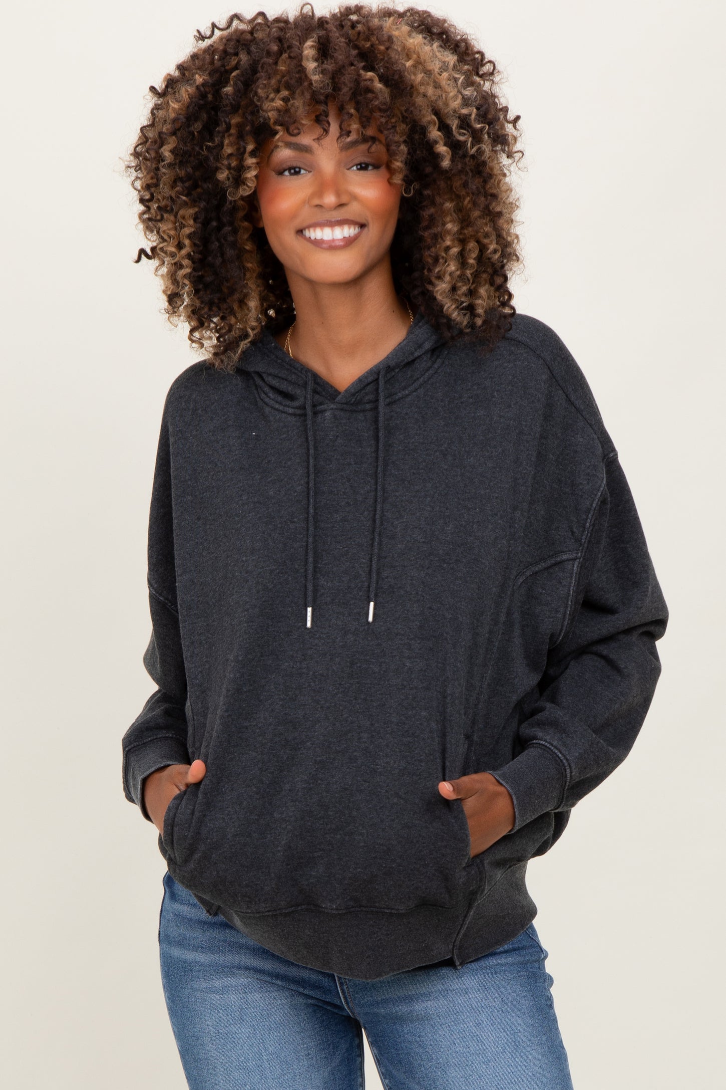 woman wearing a dark gray oversized maternity hoodie with a front pocket and hood, styled with light wash jeans