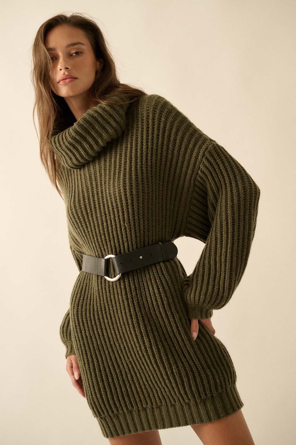 woman wearing an olive green oversized knit sweater dress with a cowl neck and black belt, posing confidently
