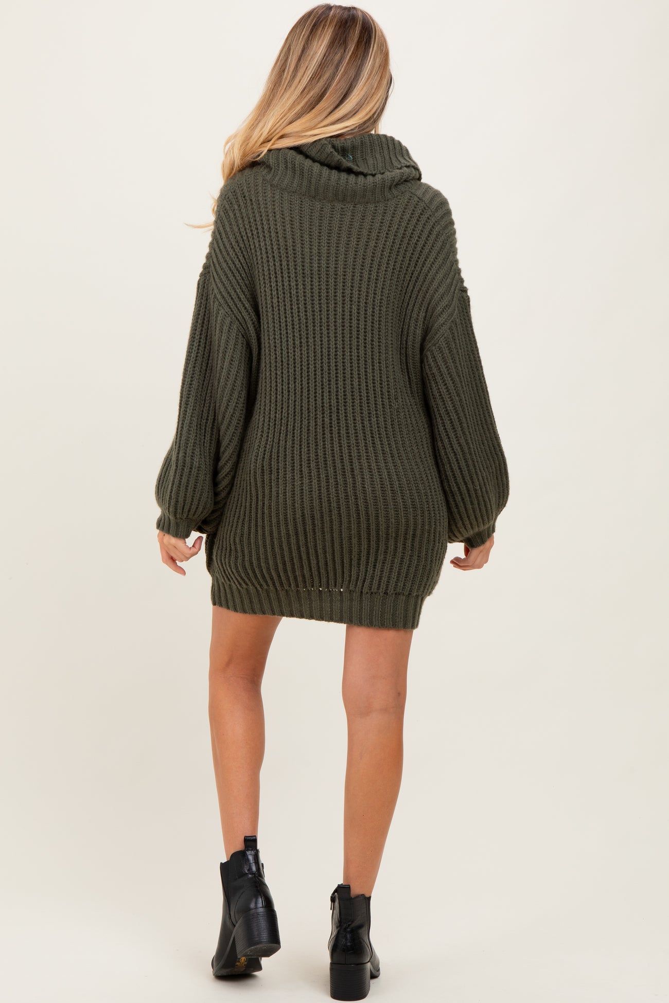 woman wearing an oversized olive green knitted maternity sweater with a cowl neck and long sleeves, facing away from the camera