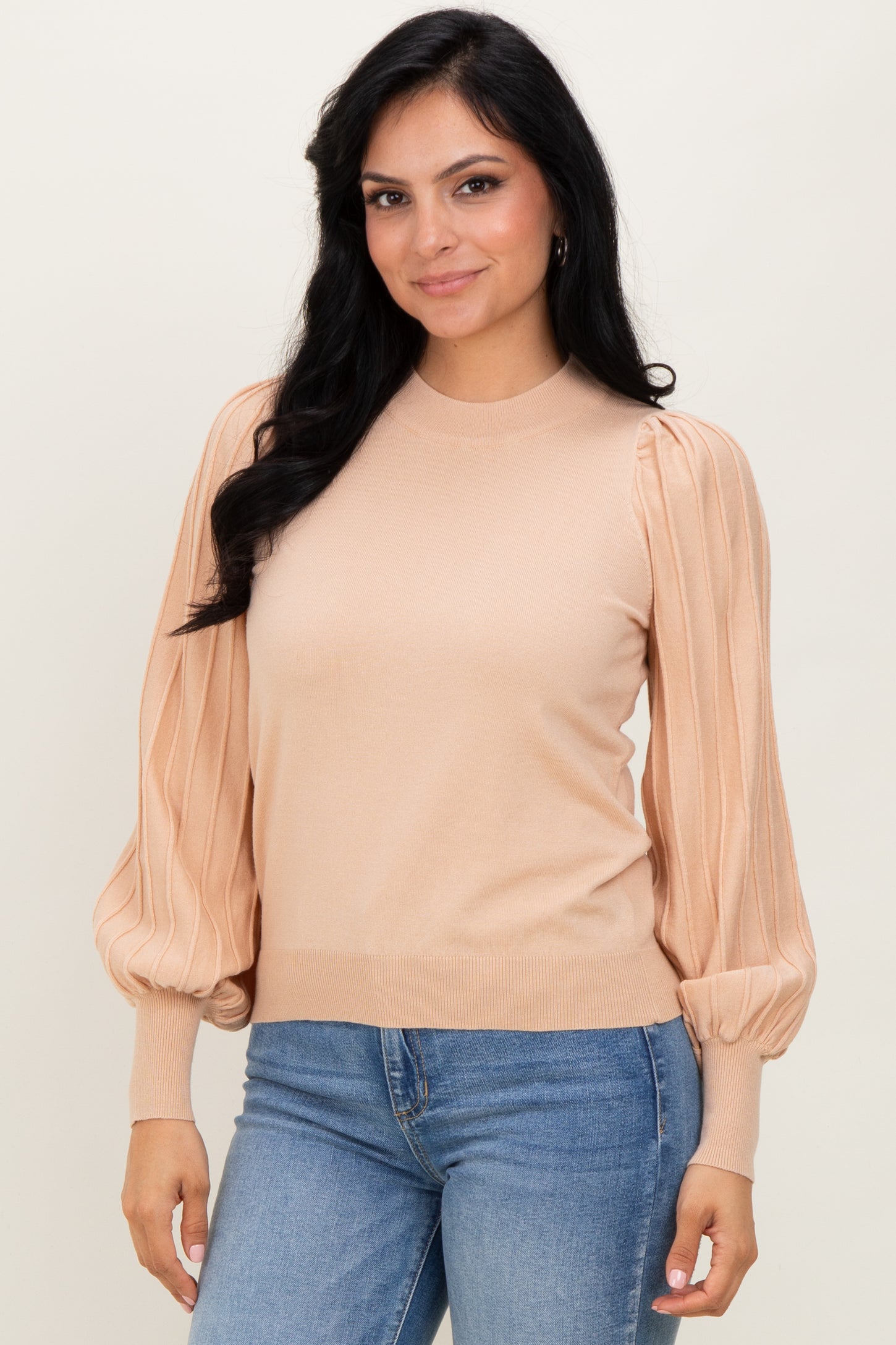 woman wearing a beige sweater with puffed sleeves, paired with blue jeans, smiling at the camera