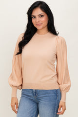 woman wearing a beige sweater with puffed sleeves, paired with blue jeans, smiling at the camera