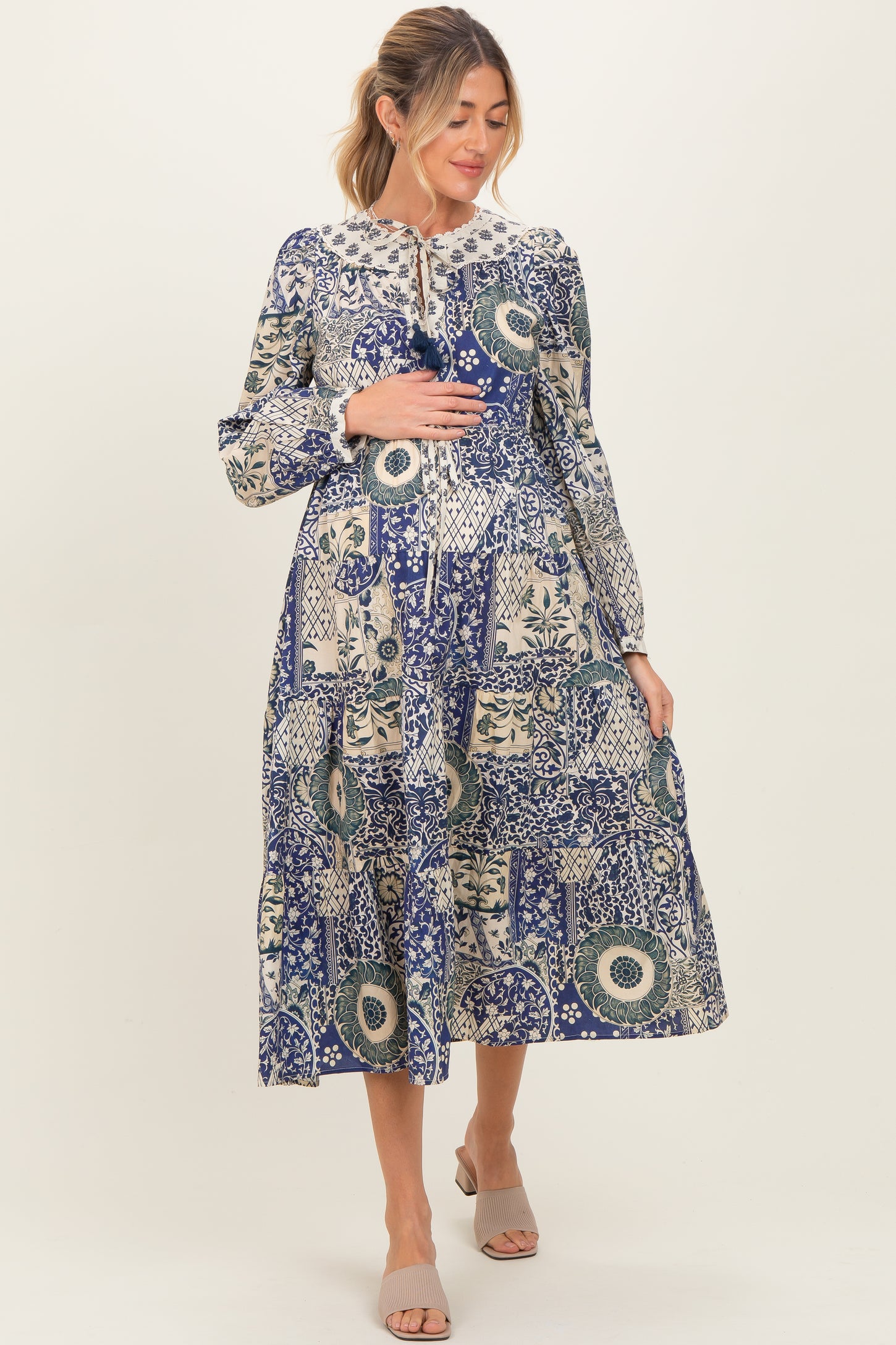 woman wearing a blue patterned maternity dress and holding her baby bump