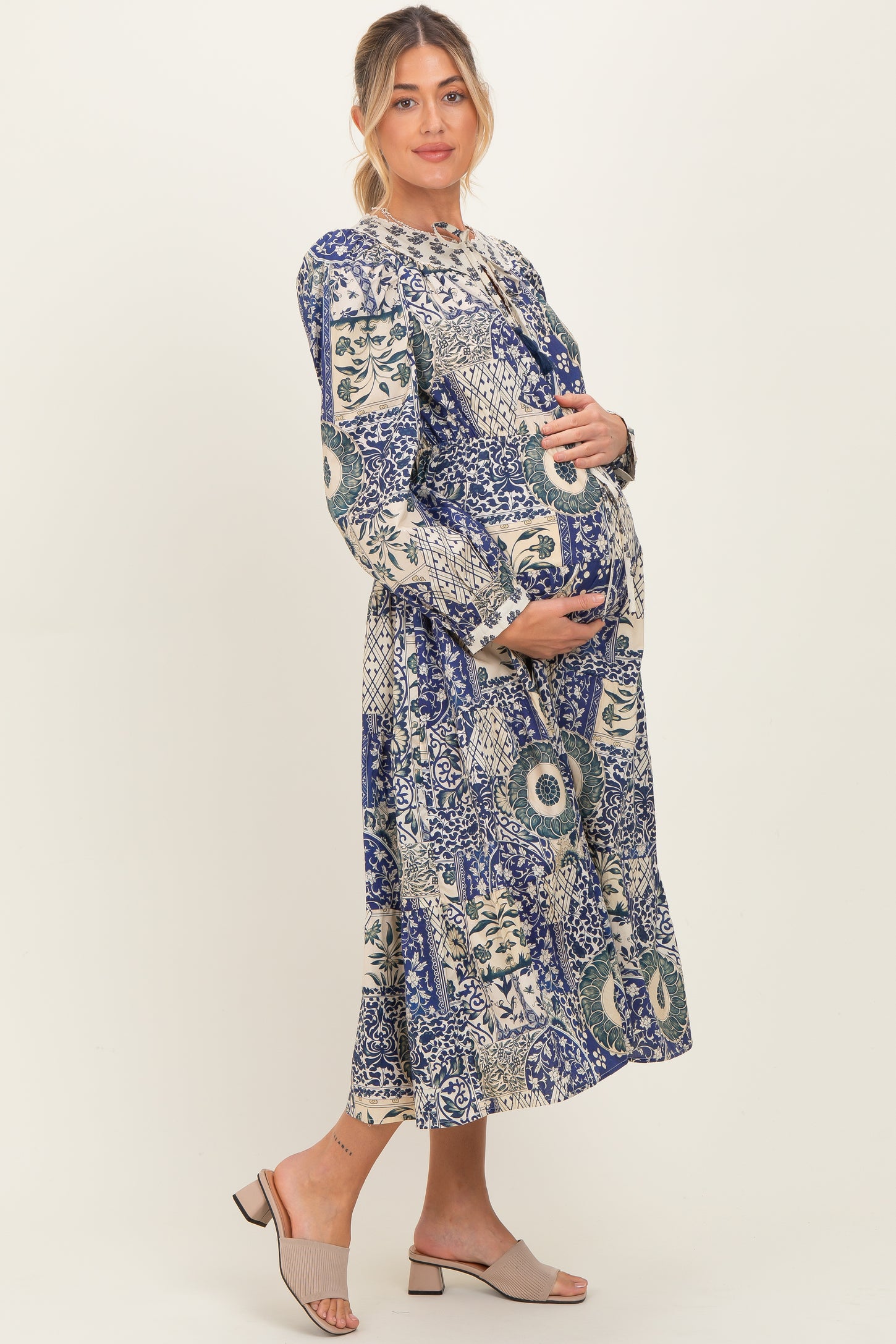 woman wearing a blue and white floral print maternity dress and holding her baby bump